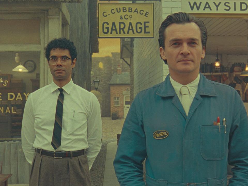 a still from the short film the rat catcher showing richard ayoade in a white shirt and black tie standing next to rupert friend in a white shirt and blue jacket