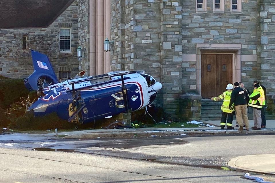 Firefighters from Upper Darby, Pa, stand near a medical helicopter that crashed next to a church in a residential area of suburban Philadelphia, Tuesday, Jan. 11, 2022, with four people on board including an infant. All are expected to survive, authorities said. [AP Photo/Claudia Lauer]