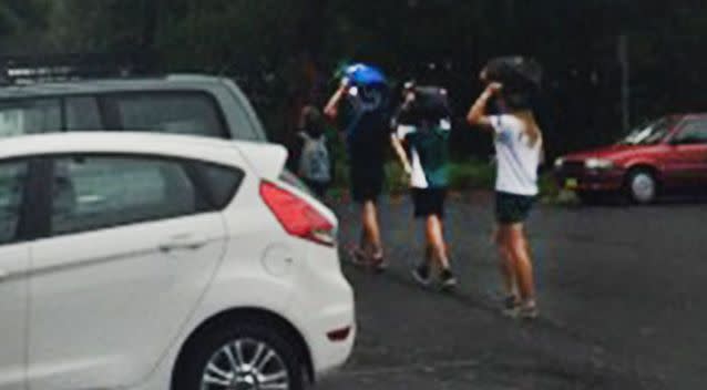 Three of Edwina Cameron's four children shelter under their school bags. Photo: Supplied