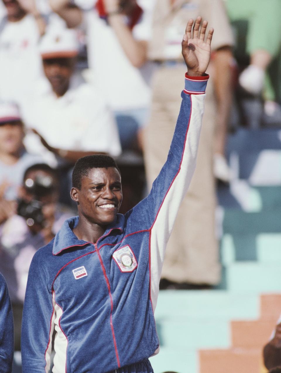 Carl Lewis in tracksuit with arm in the air in 1984.