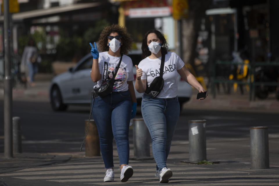 Two women wear face masks as they walk along a main street in Tel Aviv, Israel, Sunday, March 15, 2020. Prime Minister Benjamin Netanyahu announced that schools, universities, restaurants and places of entertainment will be closed to stop the spread of the coronavirus. He also encouraged people not to go to their workplaces unless absolutely necessary. (AP Photo/Oded Balilty)