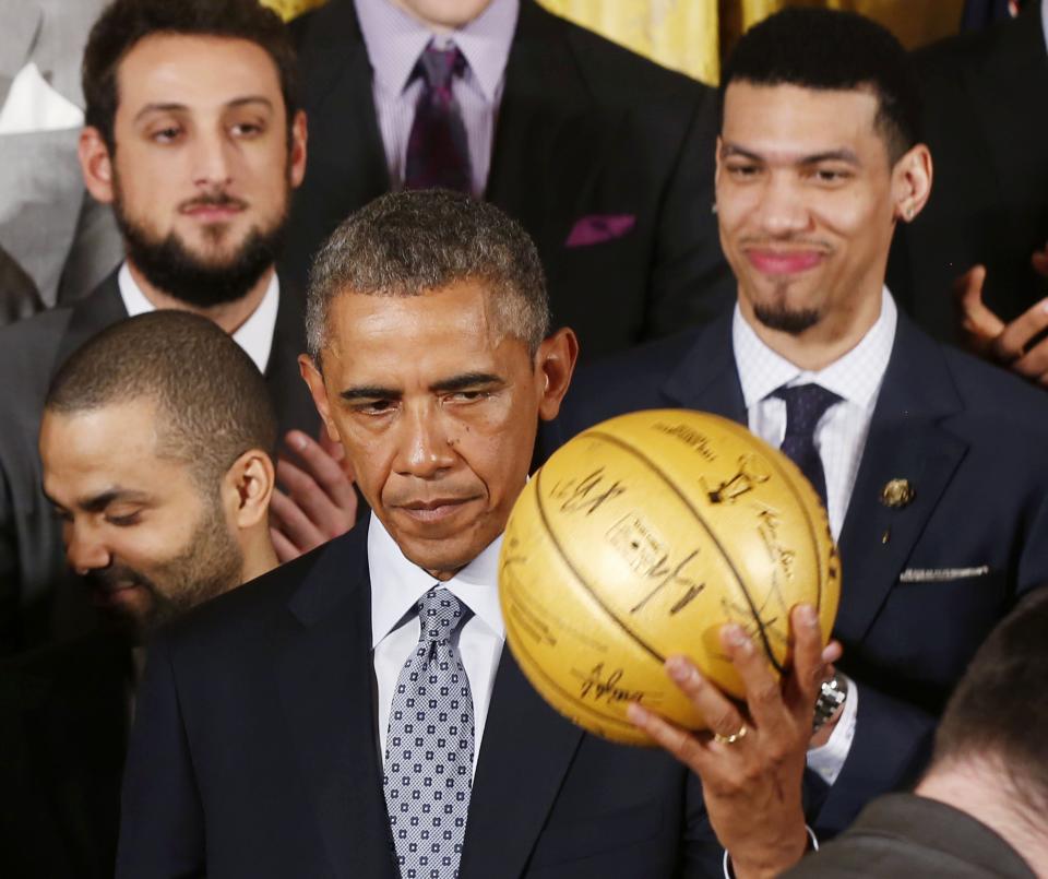 U.S. President Barack Obama holds up an autographed basketball as he welcomes the 2014 NBA Champion San Antonio Spurs to the East Room of the White House in Washington, January 12, 2015. REUTERS/Larry Downing (UNITED STATES - Tags: POLITICS SPORT BASKETBALL)