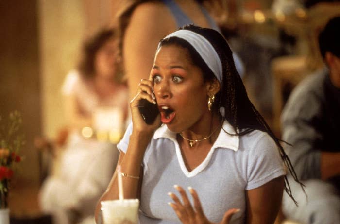 Stacey Dash talks on a phone in a shocked expression, wearing a polo shirt and headband, in a casual setting