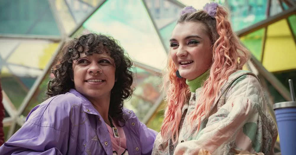 Screenshot from Sex Education with trans characters Abbi and Roman smiling.