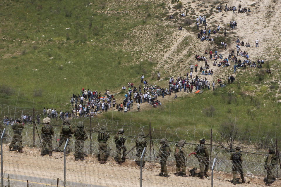 FILE - In this Sunday, June 5, 2011, file photo, Israeli troops take positions, front, as pro-Palestinian protesters approach the border between Israel and Syria near the village of Majdal Shams in the Golan Heights. Israeli troops had earlier opened fire at a crowd of protesters who tried to break into the Israeli-controlled Golan Heights from neighboring Syria in a burst of violence marking the Arab defeat in the 1967 Mideast War. (AP Photo/Oded Balilty, File)