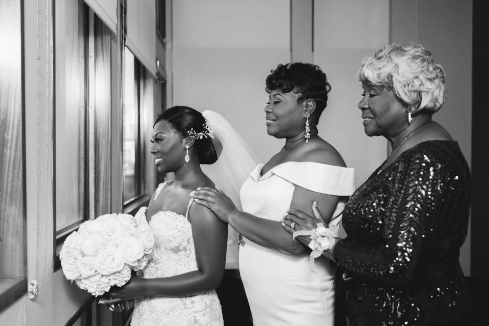 A bride, her mother, and her grandmother stand together for a photo. The photo is in black and white.