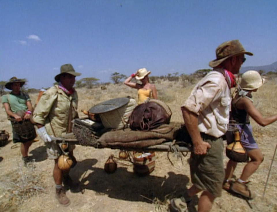 A tribe carries a pallet of supplies through the desert on Survivor: Africa