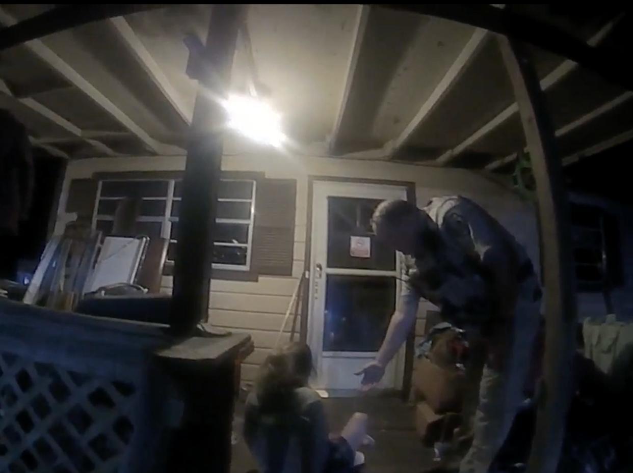 A woman sits on the ground as a deputy extends his hand