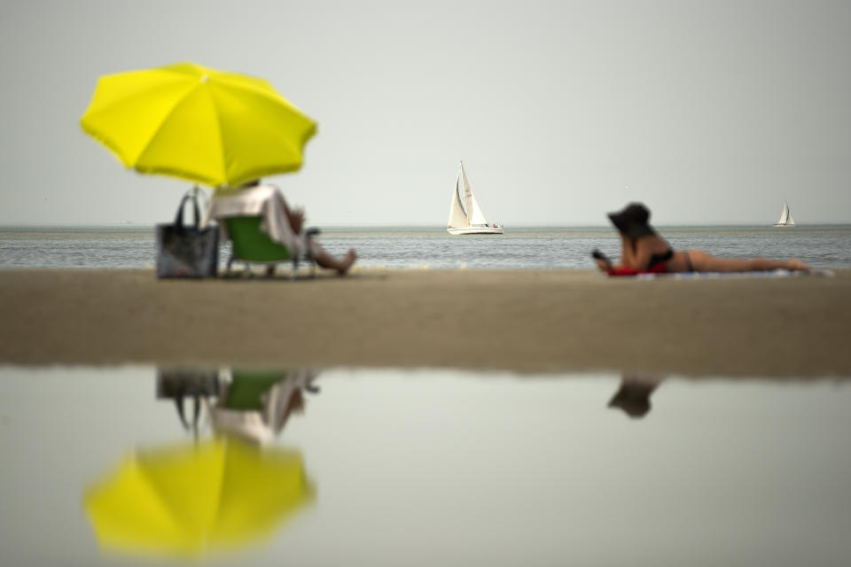 A boat sails as sunbathers relax during a hot summer day at the beach in De Haan, Belgium, Thursday, July 25, 2019. Belgium experienced code red, extreme heat warning, on Thursday as temperatures soared during the second heat wave of the summer. (AP Photo/Francisco Seco)