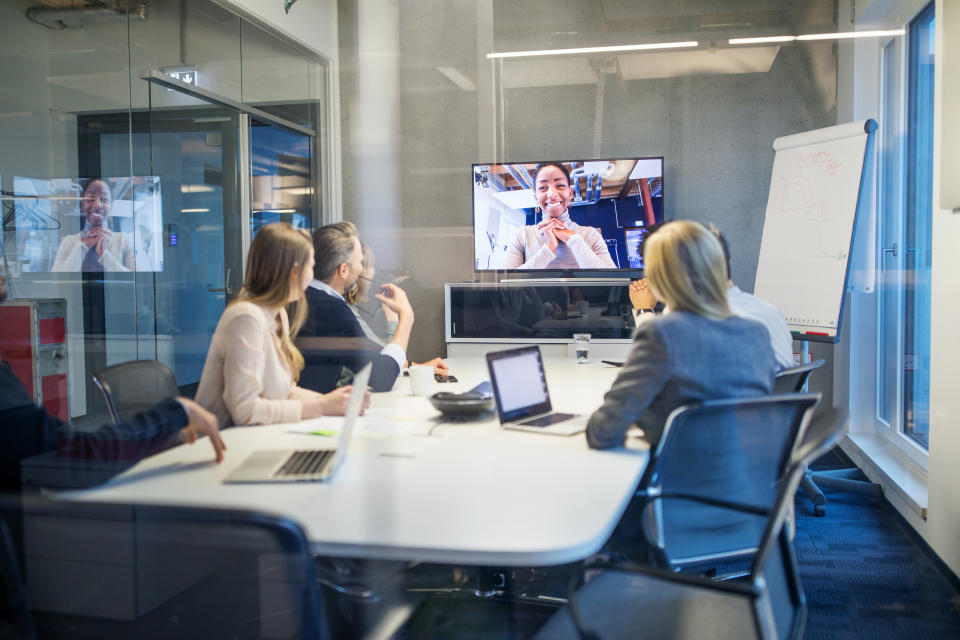 Business people looking at a screen during a video conference in the office. Businesswoman having video conference meeting with team sitting in board room.