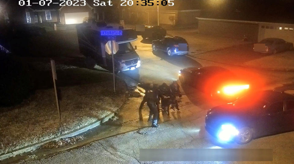 Surrounded by police patrol cars with their lights on in the dark, a cluster of officers are seen on the street. 