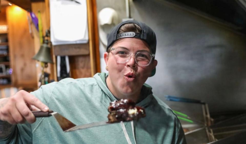 Food Network's Chef Britt Rescigno holding a "Big and Bleugie" burger, topped with blue cheese, candied jalapeno bacon, blueberry barbecue sauce and shoestring onions.