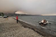 People use a dinghy as a wildfire approaches Limni village on the island of Evia, about 160 kilometers (100 miles) north of Athens, Greece, Friday, Aug. 6, 2021. Thousands of people fled wildfires burning out of control in Greece and Turkey on Friday, including a major blaze just north of the Greek capital of Athens that claimed one life, as a protracted heat wave left forests tinder-dry and flames threatened populated areas and electricity installations. (AP Photo/Thodoris Nikolaou)