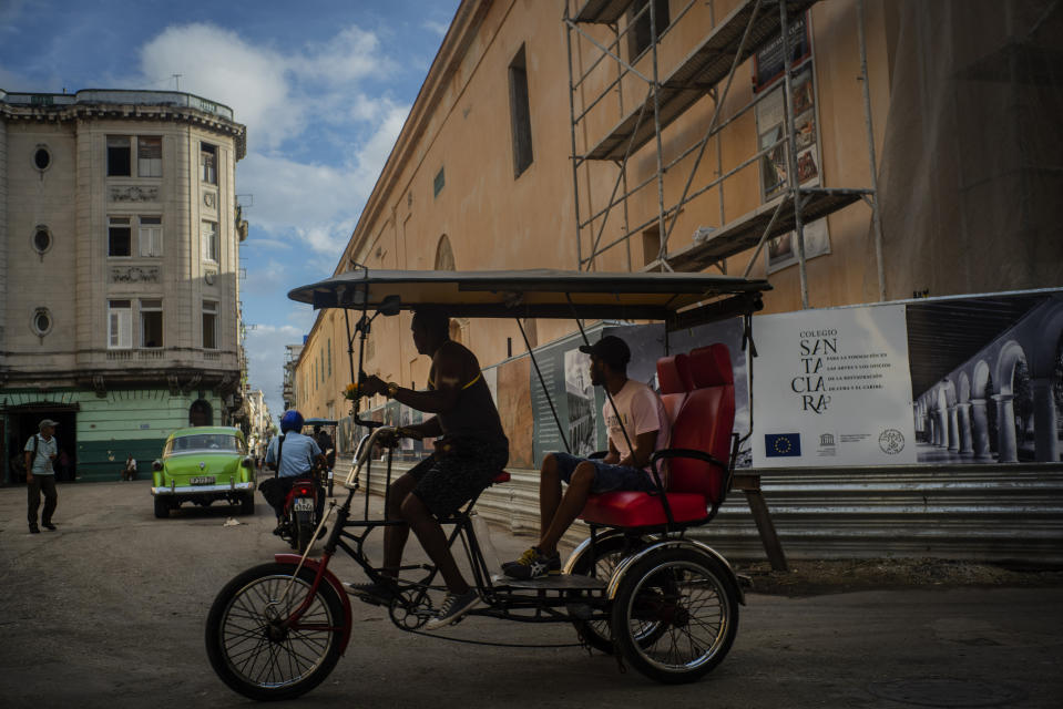 En esta foto del 9 de noviembre de 2019, un taxista de bicicleta pasea con su cliente entre edificios restaurados en La Habana, Cuba. La ciudad celebrará su 500 aniversario el 16 de noviembre. (AP Foto / Ramon Espinosa)