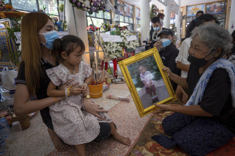 Paweenuch Supolwong, 3, the only child to emerge unscathed from the mass killing attack at the day care center, and her mother Anonpai Srithong, 35, view a victim's portrait inside Wat Rat Samakee temple in Uthai Sawan, north eastern Thailand, Saturday, Oct. 8, 2022. A former police officer burst into a day care center in northeastern Thailand on Thursday, killing dozens of preschoolers and teachers before shooting more people as he fled. (AP Photo/Wason Wanichakorn)