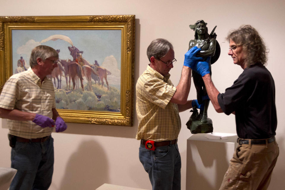 In a photo made Friday, June 28, 2013, Scott Mosher, left, Stew Henderson, center, and Michael Hudak install Hermon Atkin MacNeil's bronze statue titled "A Chief of the Multnomah Tribe" at the Colby College Museum of Art in Waterville, Maine. At left is William Herbert Dunton's oil painting, "Buffalo Signal."(AP Photo/Robert F. Bukaty)