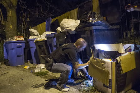 A Cook County Sheriff police officer finds a handgun hidden among the trash cans in an alley in the Austin neighborhood in Chicago, Illinois, United States, September 9, 2015. REUTERS/Jim Young