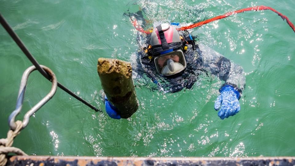 A scubadiver holds a piece of wood up to a boat