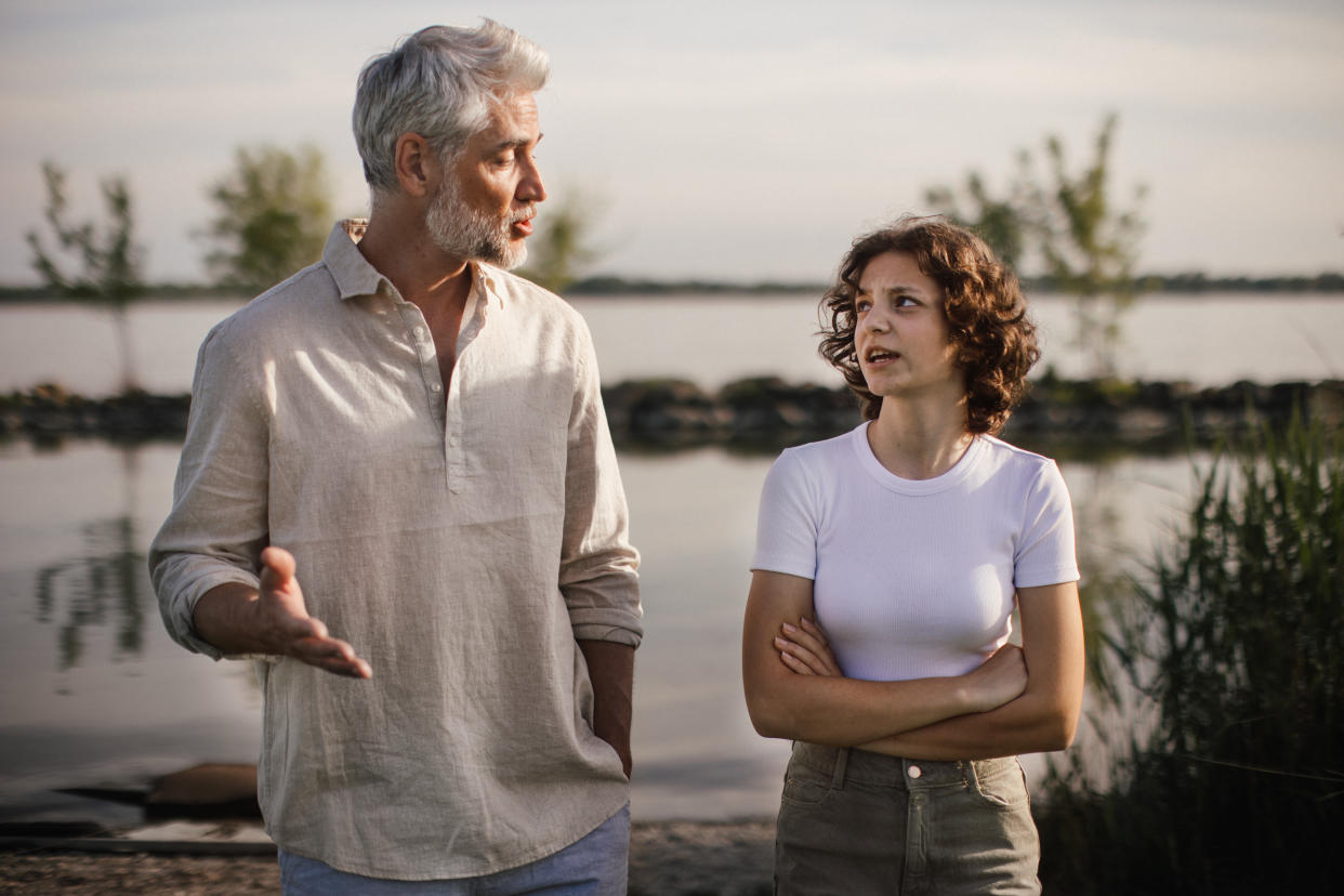 Mature man talking with his teenage girl outdoor, near lake.