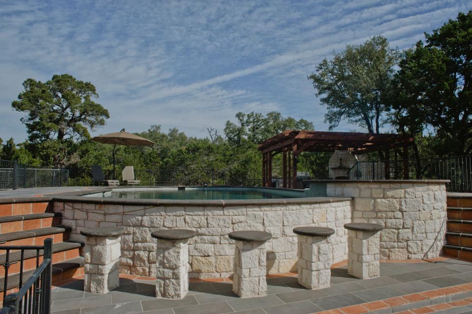 Above ground pool with a stone pool deck and wood pergola
