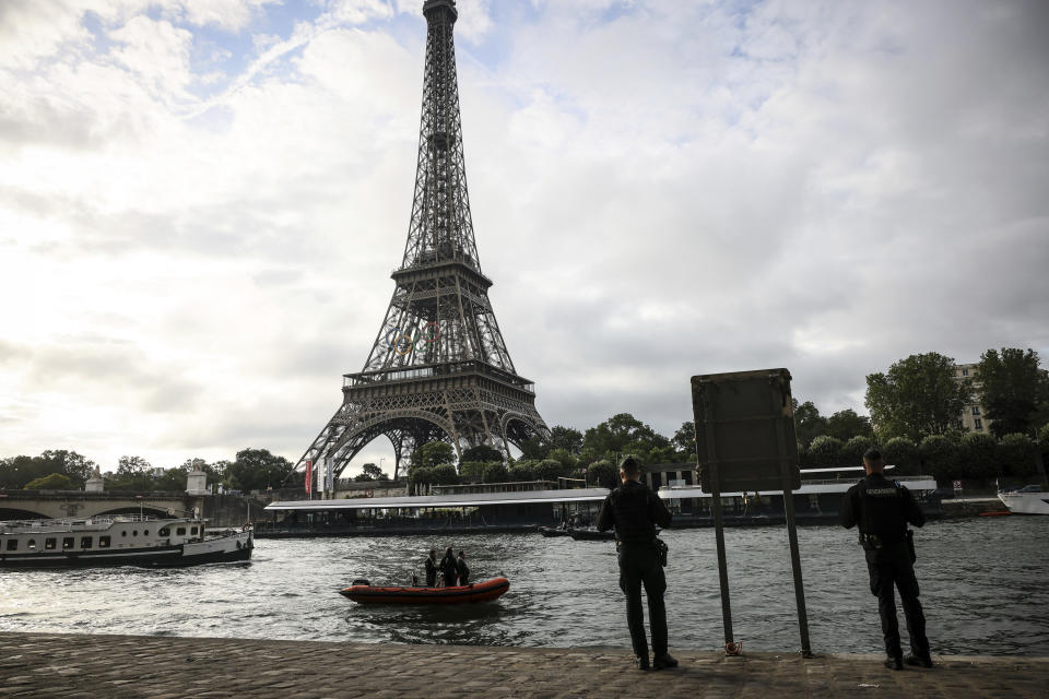 Police officers stand on the banks on the Seine river as a rescue boat and a barge cruise near the Eiffel Tower during a rehearsal for the Paris 2024 Olympic Games opening ceremony, Monday, June. 17, 2024 in Paris. The river will host the Paris 2024 Olympic Games opening ceremony on July 26 with boats for each national delegation. (AP Photo/Thomas Padilla)