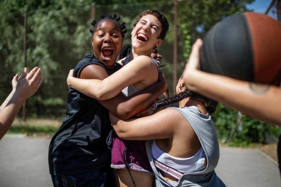 Multi-ethnic females celebrating a victory on basketball court. Women basketball team embracing each other and laughing after winning the match.