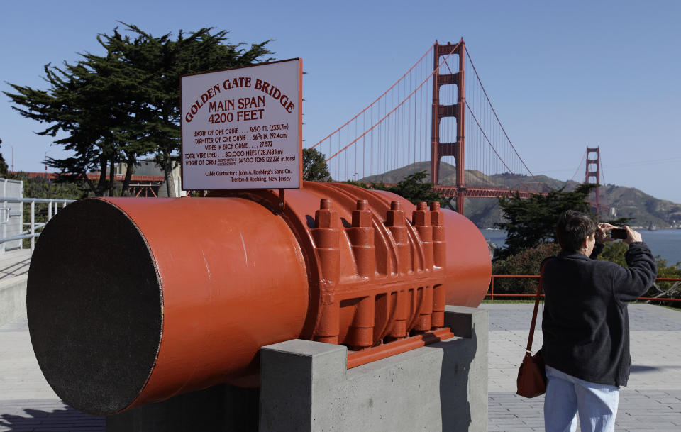 In this photo taken Thursday, May 24, 2012, a woman takes a picture from the vista point of the Golden Gate Bridge while standing next to a section of bridge cable in San Francisco. (AP Photo/Eric Risberg)
