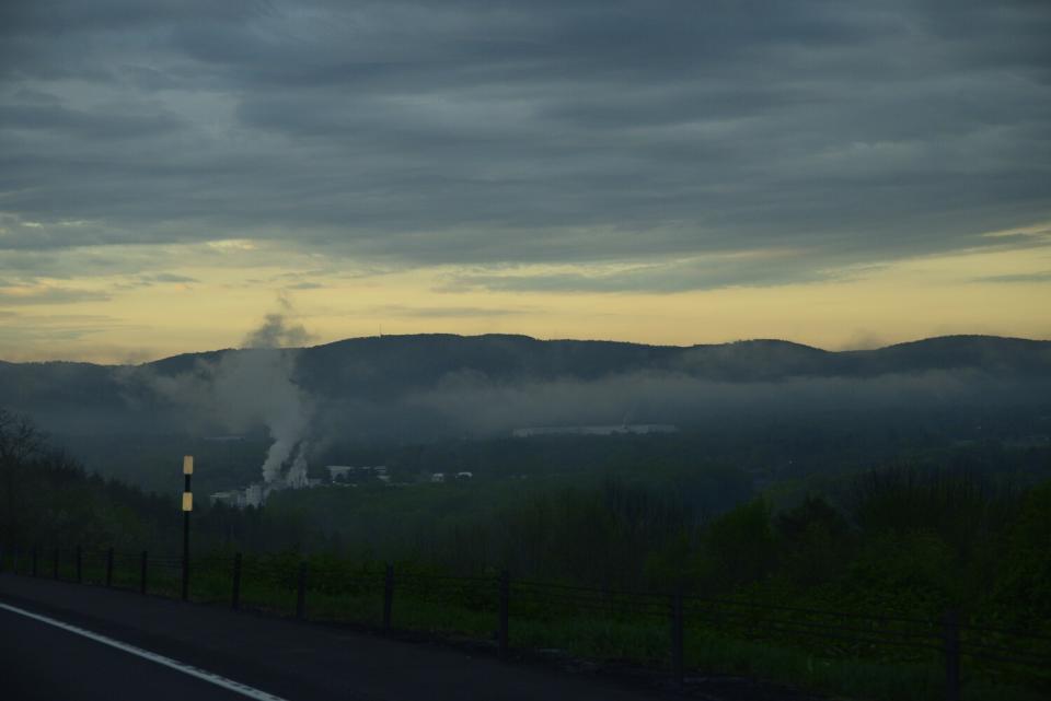 Smoke rises from a spot in a valley covered by haze.