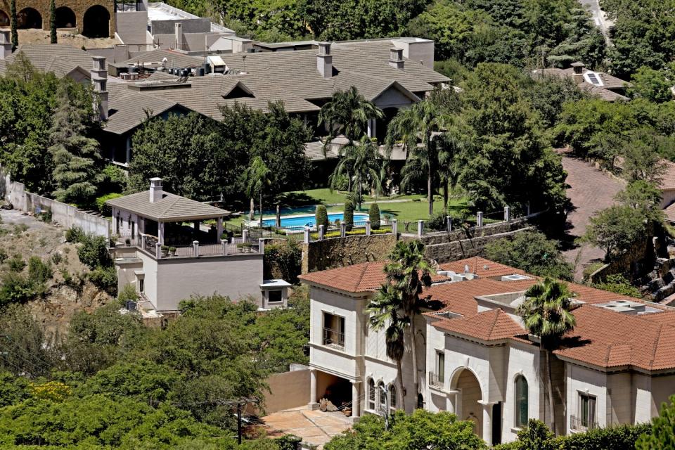 An overhead view of homes with swimming pools and green lawn and trees.