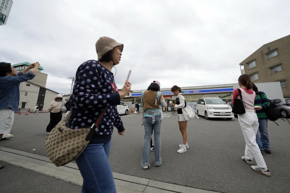 Tourists take pictures in front of the Lawson convenience store, a popular photo spot framing a picturesque view of Mount Fuji in the background on cloudy evening of Tuesday, April 30, 2024, at Fujikawaguchiko town, Yamanashi Prefecture, central Japan. (AP Photo/Eugene Hoshiko)