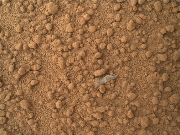 This image from the Mars Hand Lens Imager (MAHLI) camera on NASA's Mars rover Curiosity shows a small bright object on the ground beside the rover at the "Rocknest" site. The object is just below the center of this image.