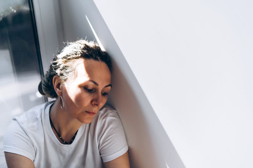 Portrait of a dreadlocks braid topknot bun woman in white T-shirt next the white wall with hard shadow.