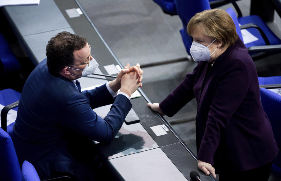 German Federal Minister of Health Jens Spahn, left, and Chancellor Angela Merkel talk while wearing a face masks on the government benches during the current affairs hour of the plenary session in the German federal parliament, Bundestag, at the Reichstag building in Berlin, Germany, Wednesday, Jan. 27, 2021. (Bernd von Jutrczenka/dpa via AP)