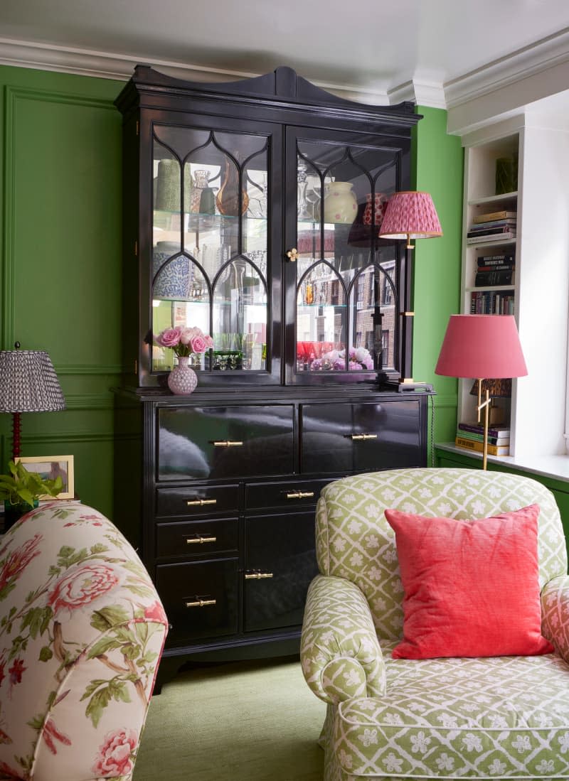 Black dining cabinet against green wall behind chairs.