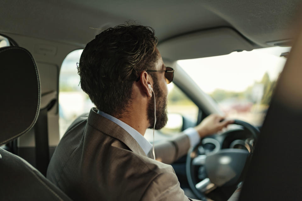 A handsome businessman in a full suit wearing headphones while driving his car. 