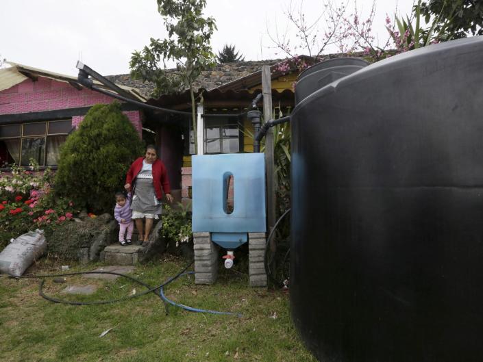 woman and small child stand on house front steps next to blue and black rainwater tanks