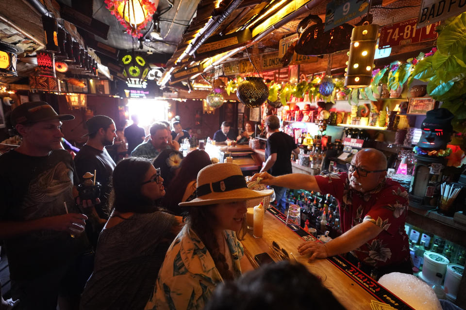 FILE - In this Wednesday, July 7, 2021, file photo, patrons enjoy cold tropical cocktails in the tiny interior of the Tiki-Ti bar as it reopens on Sunset Boulevard in Los Angeles. COVID-19 cases have doubled over the past three weeks, driven by the fast-spreading delta variant, lagging vaccination rates in some states and Fourth of July gatherings. Los Angeles County public health officials have urged people to resume wearing masks indoors regardless of their vaccination status. (AP Photo/Damian Dovarganes, File)