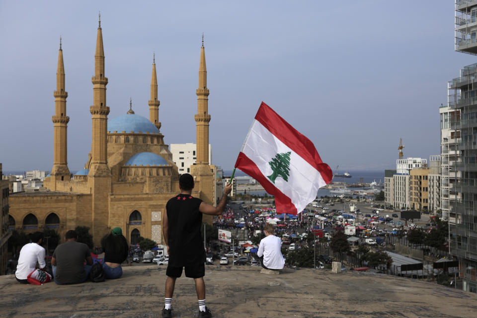 An anti-government protester holds up a Lebanese national flag during a protest in Beirut, Lebanon, Friday, Oct. 25, 2019. Leader of Lebanon's Hezbollah calls on his supporters to leave the protests to avoid friction and seek dialogue instead. (AP Photo/Hassan Ammar)