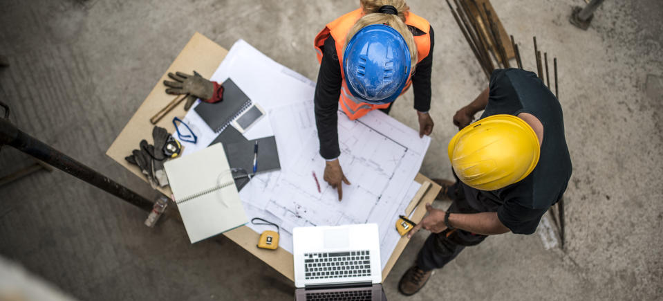 Image of two construction workers examining blueprints next to a laptop to represent tech on construction sites.