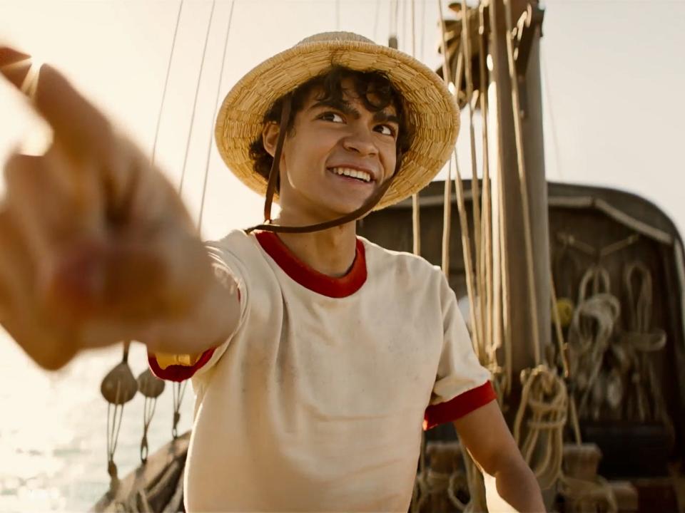 iñaki godoy as luffy in one piece, sitting on a boat and pointing forward with a smile on his face