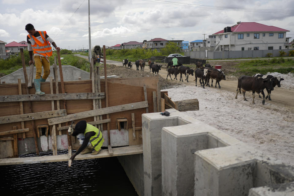 Workers build a road through the Mocha Arcadia area of Georgetown, Guyana, Friday, April 14, 2023. With $1.6 billion in oil revenue so far, the government has launched infrastructure projects including the construction of 12 hospitals, seven hotels, scores of schools, two main highways, its first deep-water port and a $1.9 billion gas-to-energy project. (AP Photo/Matias Delacroix)