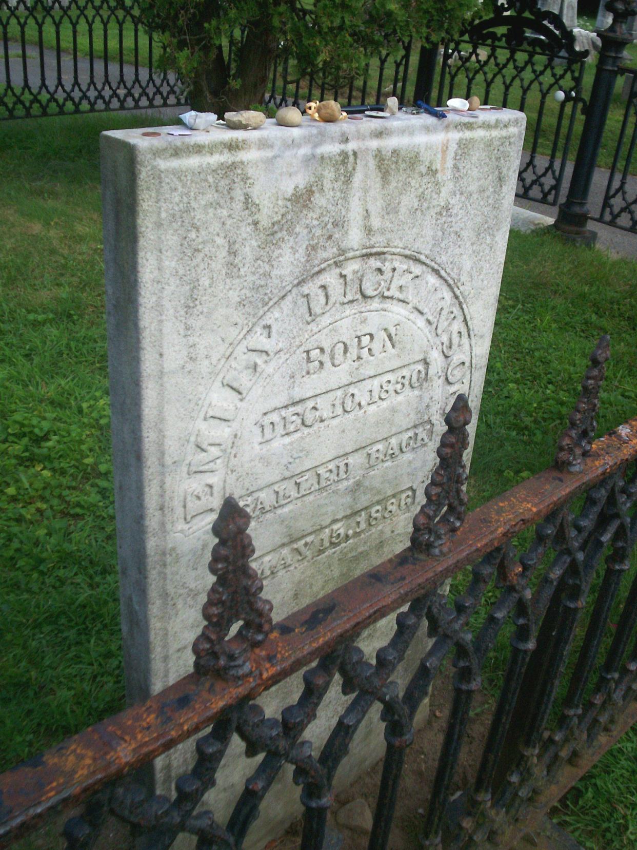 Emily Dickinson's grave in the Amherst West Cemetery, Amherst, Massachusetts, several crystals on top of headstone, behind an elaborate black fence with grass lawn and rest of black fence in the background