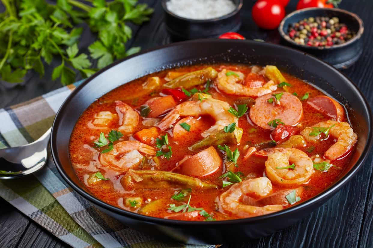 Delicious gumbo with prawns, baby okra and sausage in a bowl on a black table with napkin and silver spoon,  view from above, close-up