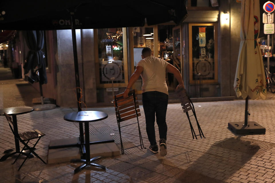 An owner of the Beers Bank pub removes chairs and tables from the terrace of the bar at the end of the day in Brussels, Wednesday, Oct. 7, 2020. Since bars in Brussels were forced to close as of Thursday for at least a month to deal with a massive surge in cases while restaurants were allowed to remain open, the big question on the streets is: when is a bar a bar and when is a bar a restaurant. (AP Photo/Francisco Seco)