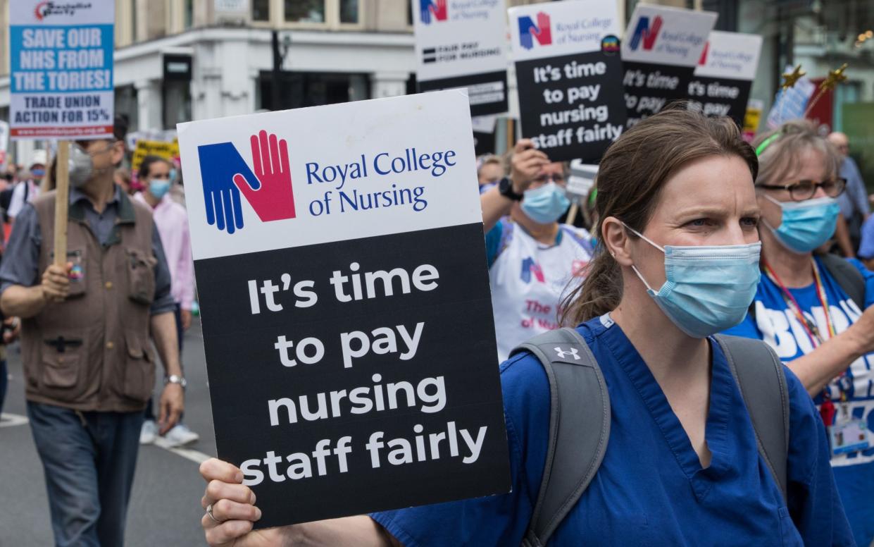 Nurses in scrubs hold up signs demanding fair pay during a march - Mark Kerrison/Getty Images