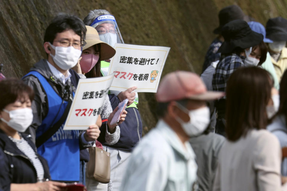 Organizers hold signs to spectators that read: "Avoid crowding! Wear masks" during the Tokyo Olympic torch relay in Tobe, Ehime prefecture, southwestern Japan, Thursday, April 22, 2021. Tokyo Olympic organizers said Thursday that a Japanese policeman tested positive for COVID-19 a day after his assignment of traffic control at the April 17 leg of the torch relay. It is the first positive test report connected to the relay since it kicked off on March 25. (Kyodo News via AP)