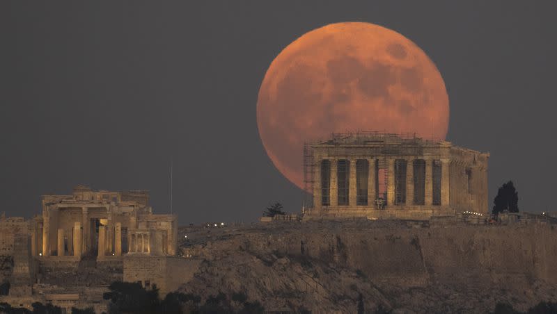 The full moon rises behind the Acropolis hill and the ancient Parthenon temple, in Athens, Greece, on Tuesday, Nov. 8, 2022.