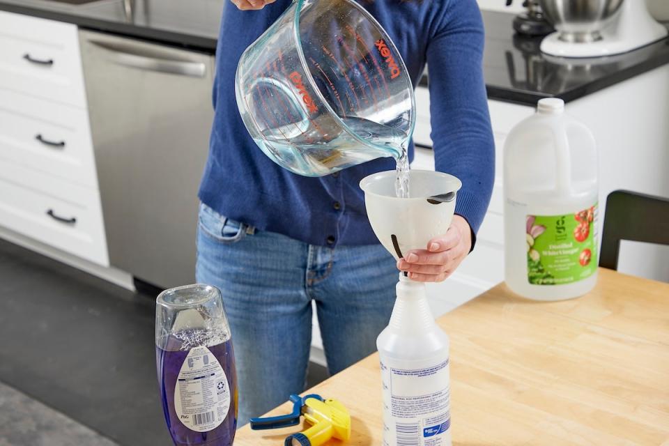 A person pouring water into a spray bottle to make homemade window cleaner for the house.