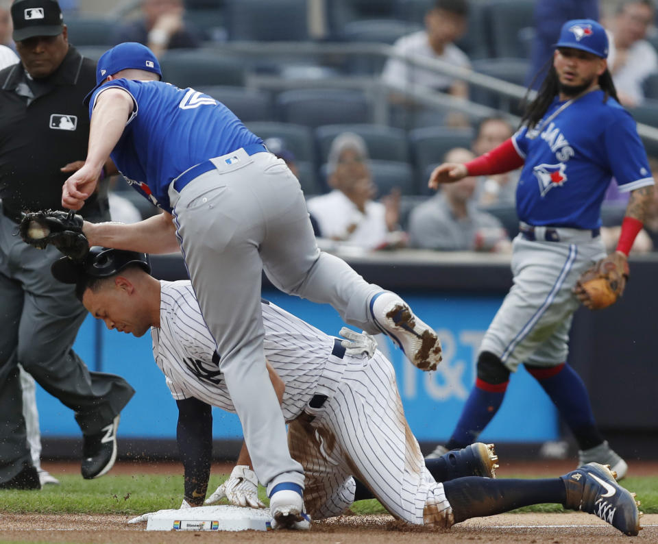 Toronto Blue Jays starting pitcher Clayton Richard (2) steps over New York Yankees' Giancarlo Stanton after tagging Stanton out at third on a double play during the first inning of a baseball game, Tuesday, June 25, 2019, in New York. Stanton left after the third inning. Blue Jays shortstop Freddy Galvis backs up the play, right. Umpire Laz Diaz is at left rear. (AP Photo/Kathy Willens)