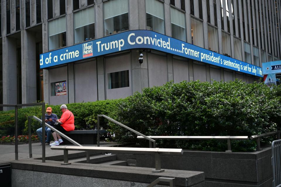 People sit under a digital billboard at the Fox News Corporation building announcing that former President and Republican presidential candidate Donald Trump had been convicted in his criminal trial in New York City on May 30, 2024.